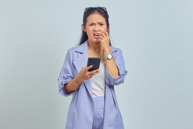 Ritratto di giovane donna asiatica che utilizza il telefono cellulare che sembra stressato e nervoso con la mano in bocca che morde il chiodo su sfondo bianco