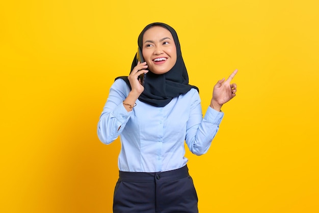 Ritratto di giovane donna asiatica felice che parla al telefono cellulare isolato su sfondo giallo