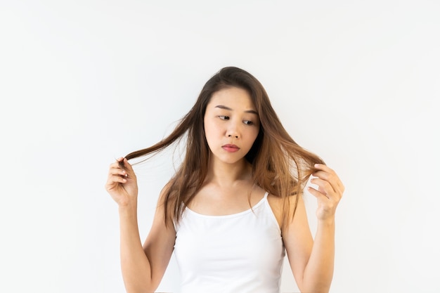 Ritratto di giovane donna asiatica frustrata con capelli castani scompigliati sul muro bianco. Avvicinamento.