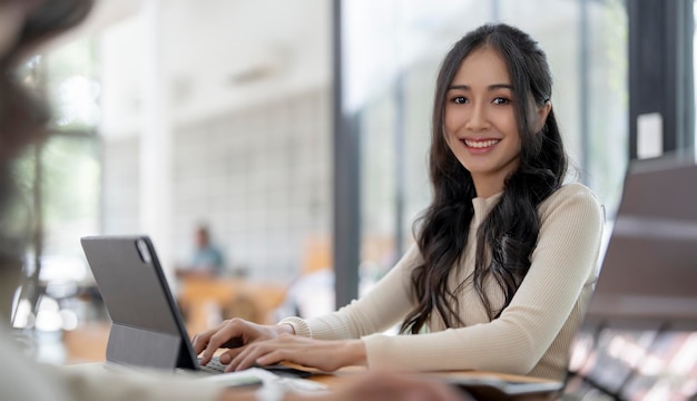 Ritratto di giovane donna asiatica intelligente freelance che lavora online da casa con il laptop sorridente e guardando il camer