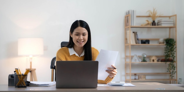 Ritratto di giovane donna asiatica libero professionista sta lavorando il suo lavoro su tablet computer in casa moderna facendo analisi contabile report dati di investimento immobiliare Concetto di sistemi finanziari e fiscali