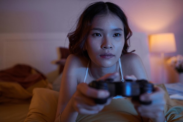 Ritratto di giovane donna asiatica sdraiata sul letto e giocare al videogioco a tarda notte