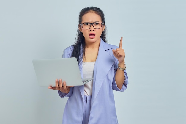 Ritratto di giovane donna asiatica sorpresa in piedi utilizzando il laptop e puntando il dito contro lo spazio della copia con la bocca aperta isolata su sfondo bianco