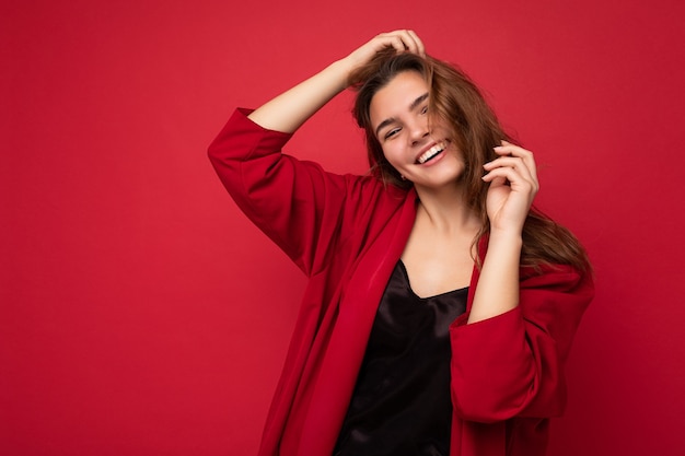 Ritratto di giovane donna attraente caucasica hipster in abiti casual alla moda. Persona di sesso femminile spensierata sexy in posa isolata vicino alla parete rossa in studio. Spazio vuoto.