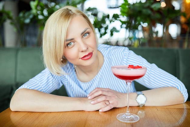 Ritratto di giovane donna attraente che beve cocktail nella caffetteria al coperto Bella donna bionda rilassante al bar e bere un cocktail
