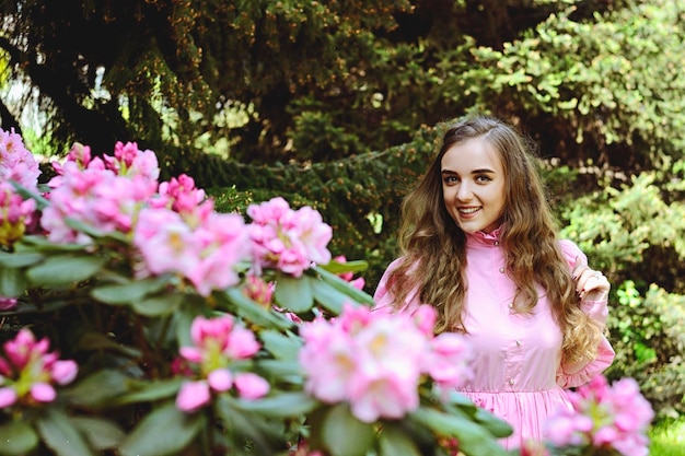 Ritratto di giovane donna attraente in abito da sposa bianco lungo nel giardino di primavera con alberi in fiore.