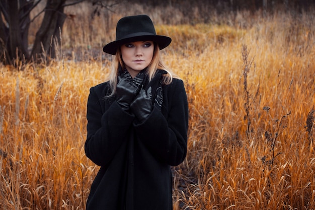 Ritratto di giovane donna attraente in cappotto nero e cappello.