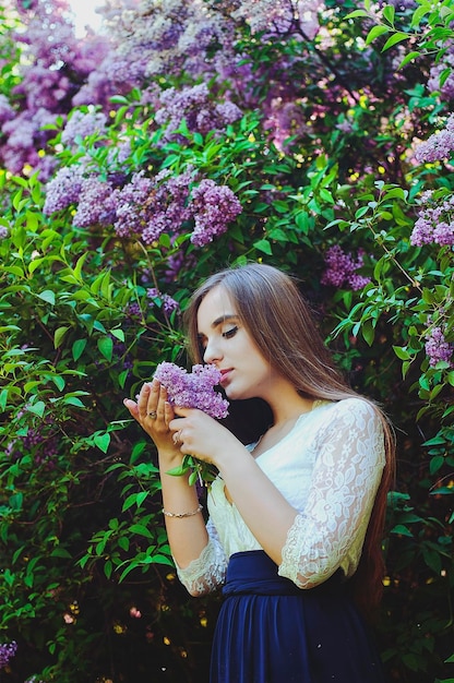 Ritratto di giovane donna attraente in giardino primaverile con un mazzo di lillà. Sfondo primaverile.