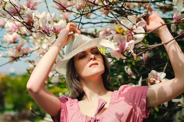 Ritratto di giovane donna attraente nel giardino primaverile con magnolie rosa in fiore. Sfondo primaverile