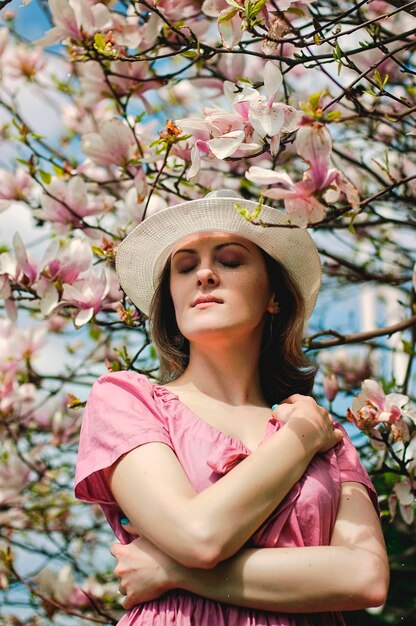 Ritratto di giovane donna attraente nel giardino primaverile con magnolie rosa in fiore. Sfondo primaverile