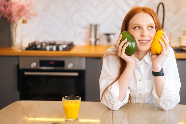 Ritratto di giovane donna attraente rossa sognante affascinante che tiene in mano mango e avocado