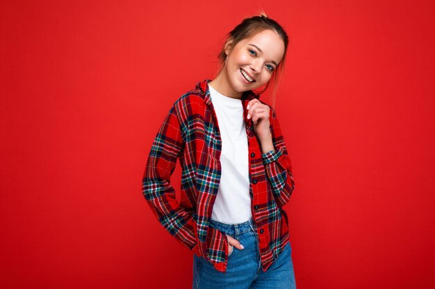 Ritratto di giovane donna bionda sorridente attraente dei pantaloni a vita bassa in camicia rossa alla moda e bianco casuale