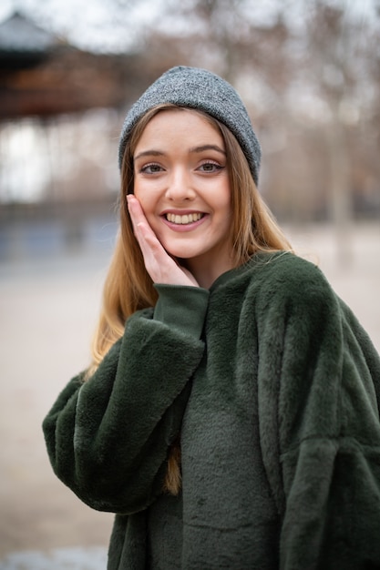 Ritratto di giovane donna bionda sorridente felice con il cappello di inverno in un parco in autunno