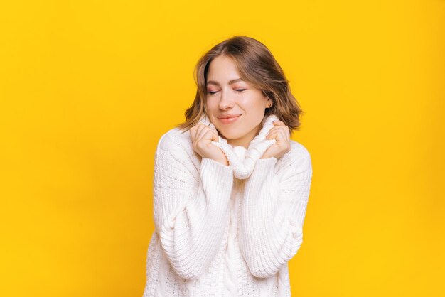 Ritratto di giovane donna carina che indossa un maglione bianco su sfondo giallo