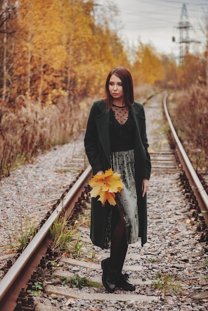 Ritratto di giovane donna carina di aspetto slavo in abbigliamento casual in autunno, su strada ferroviaria sullo sfondo di un parco e di un fiume autunnali. Bella donna che cammina nella foresta in autunno dorato. Copia spazio