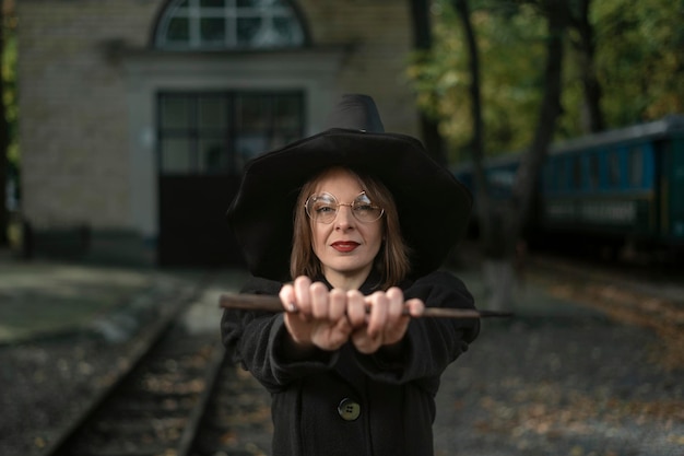 Ritratto di giovane donna carismatica in costume da strega tiene una festa di Halloween davanti alla sua Scuola di Magia