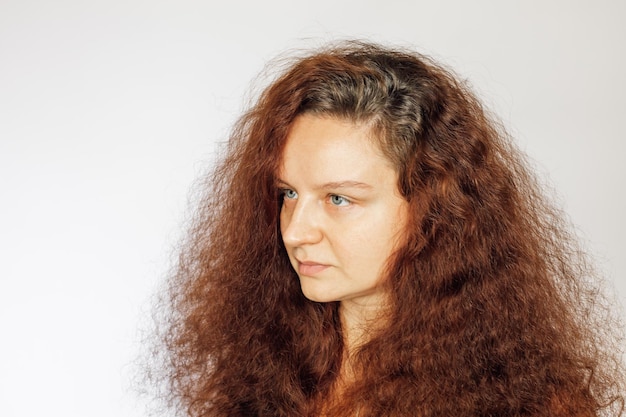 Ritratto di giovane donna caucasica con lussureggianti capelli ondulati colorati in rosso pelle del viso pulita e morbida senza trucco occhi che distolgono lo sguardo su sfondo bianco Accettazione di sé