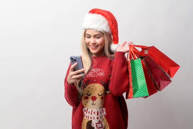 Ritratto di giovane donna caucasica felice in cappello di Babbo Natale con borse della spesa su sfondo bianco