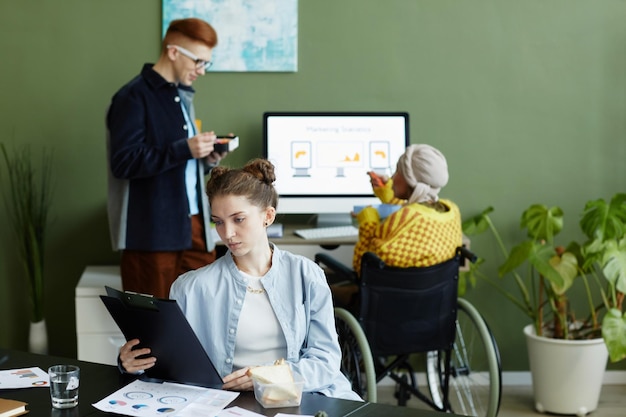 Ritratto di giovane donna che analizza i dati mentre lavora con il team creativo in ufficio