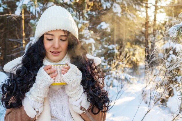 Ritratto di giovane donna che beve bevanda calda nella foresta di inverno