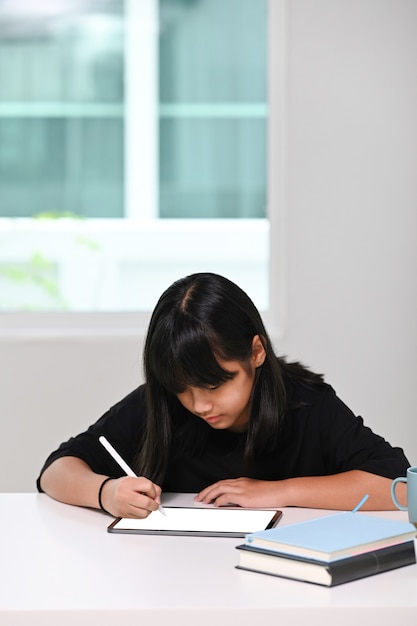 Ritratto di giovane donna che fa i compiti sulla tavoletta digitale a casa. Formazione in linea, apprendimento a casa, concetto di homeschooling.