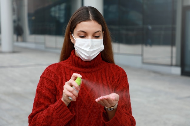 Ritratto di giovane donna che indossa la mascherina medica protettiva spruzzare disinfettante alcolico sulle sue mani