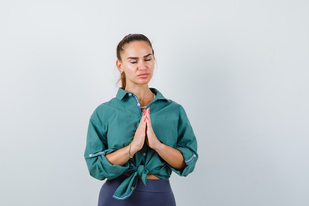 Ritratto di giovane donna che mostra il gesto di namaste in camicia verde e sembra una vista frontale speranzosa