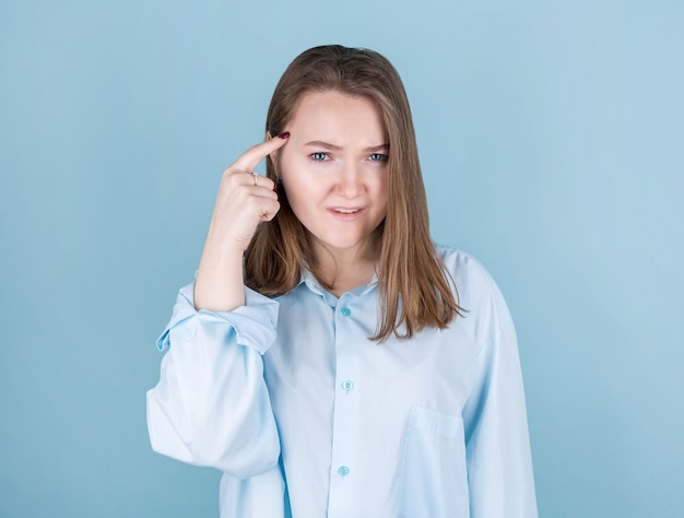 Ritratto di giovane donna che pensa con il dito alla testa isolato sull'azzurro