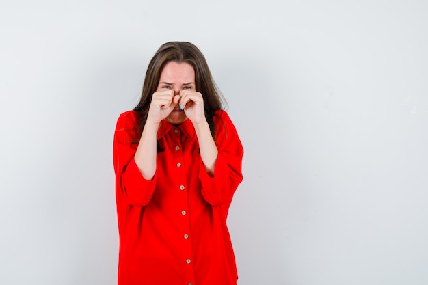 Ritratto di giovane donna che si asciuga le lacrime con le mani in una camicetta rossa e sembra depressa vista frontale