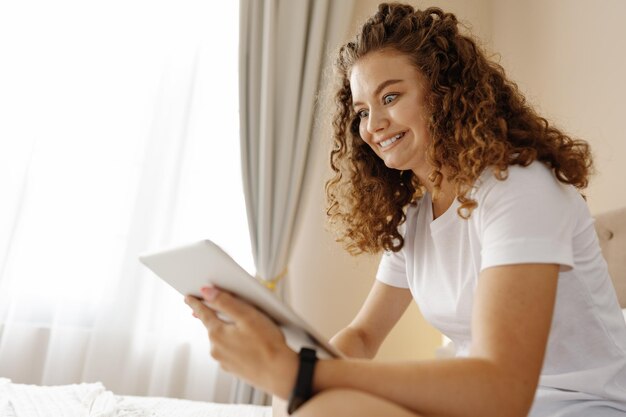 Ritratto di giovane donna che utilizza la moderna tavoletta digitale seduta su un letto