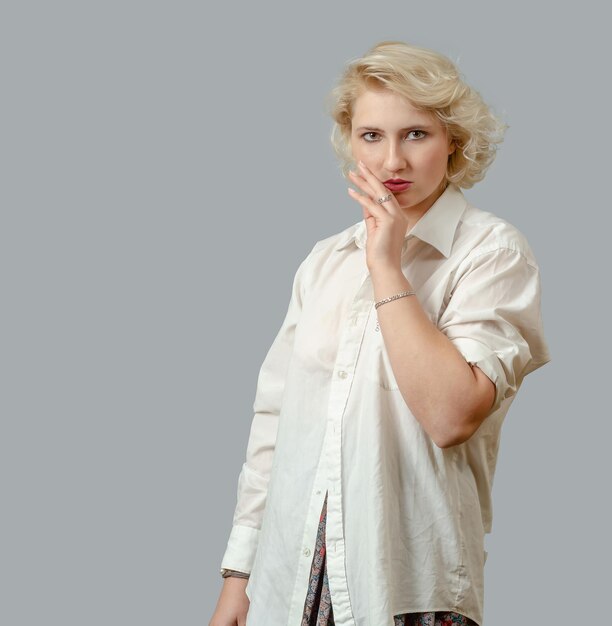 Ritratto di giovane donna con capelli biondi corti in camicia bianca si sente insicuro davanti alla telecamera