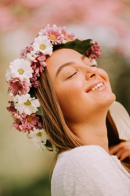 Ritratto di giovane donna con la corona di fiori freschi sulla testa nel parco