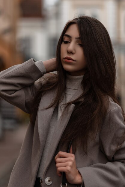 ritratto di giovane donna con lunghi capelli castani in un cappotto alla moda in posa in città