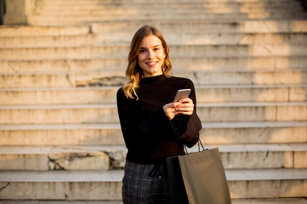 Ritratto di giovane donna con shopping bag e telefono cellulare all&#39;aperto