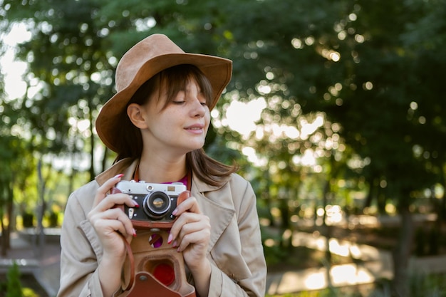 Ritratto di giovane donna di moda in cappello di feltro con fotocamera retrò nel parco cittadino