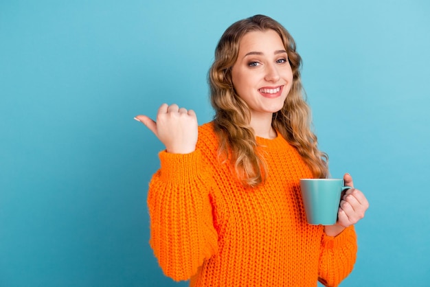 Ritratto di giovane donna divertente allegra punto tenere tazza di carta caffè tè guardando da parte isolato su sfondo di colore blu studio