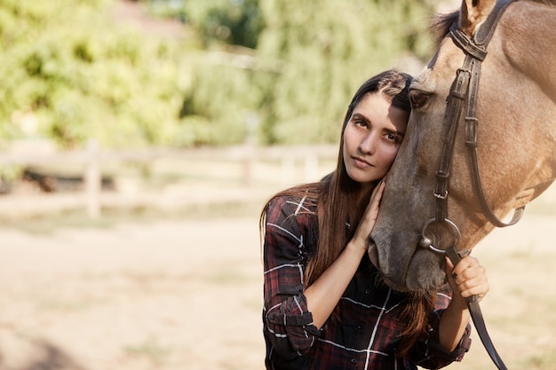 Ritratto di giovane donna e un cavallo. Bella ragazza dai capelli lunghi che tiene e che calma uno stallone.