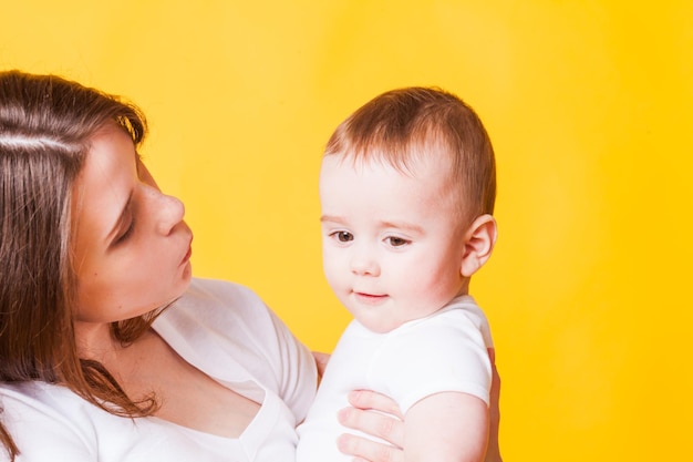 Ritratto di giovane donna e un piccolo bambino, isolato su sfondo giallo. Madre che cerca di baciare suo figlio, concetto