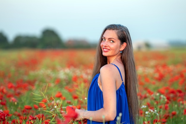 Ritratto di giovane donna elegante con i capelli lunghi in un campo di papaveri alla luce del sole serale