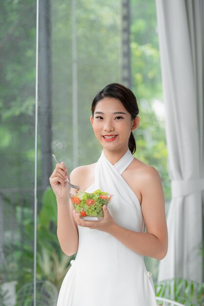 Ritratto di giovane donna felice che mangia insalata di verdure