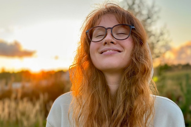 Ritratto di giovane donna felice in vetri al tramonto su sfondo naturale sorriso e rivolto verso l'obiettivo