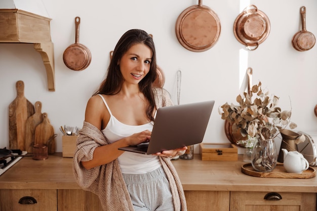 Ritratto di giovane donna freelance che utilizza laptop e lavora in cucina
