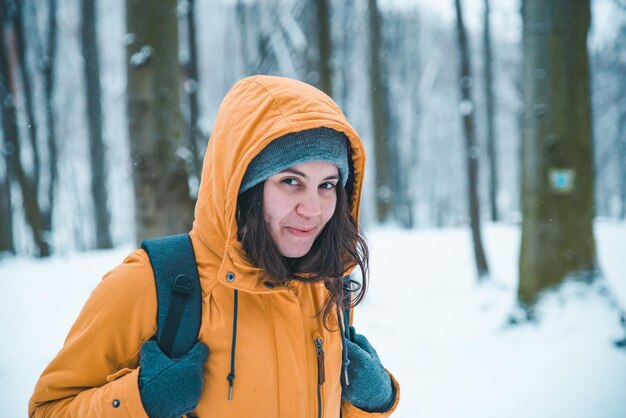 Ritratto di giovane donna graziosa in cappotto con cappuccio nella foresta innevata