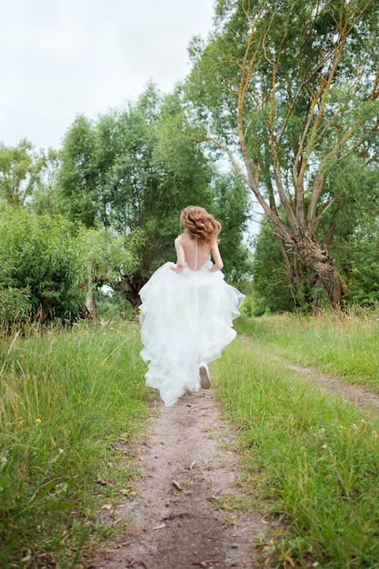 Ritratto di giovane donna graziosa (sposa) in abito da sposa bianco all'aperto scappando