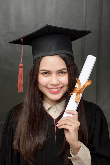 Ritratto di giovane donna in abito di laurea sorridente e tifo su sfondo nero