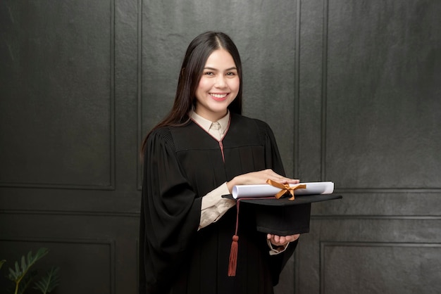 Ritratto di giovane donna in abito di laurea sorridente e tifo su sfondo nero