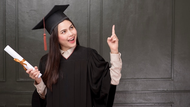 Ritratto di giovane donna in abito laurea sorridente e tifo su sfondo nero