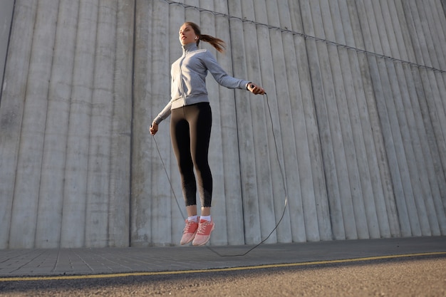 Ritratto di giovane donna in forma con corda per saltare all'aperto. Fitness femminile facendo saltare l'allenamento all'aperto all'alba o al tramonto.