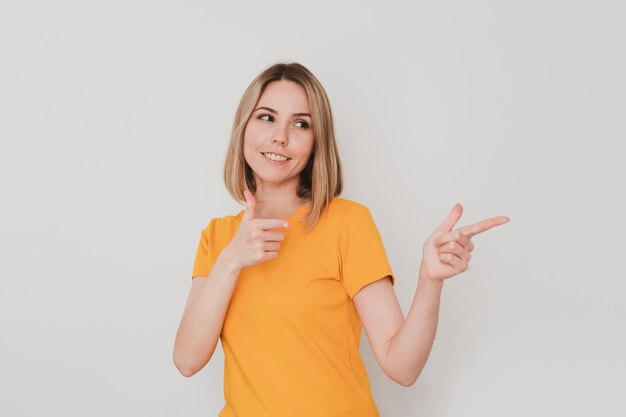 Ritratto di giovane donna in maglietta gialla che punta il dito di lato. Su sfondo bianco. Gesti delle mani