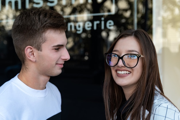 Ritratto di giovane donna in occhiali alla moda e uomo per strada. Amanti felici.